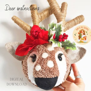 以下が含まれることがあります： 茶色と白の顔、赤い花、緑のヒイラギが付いたフェルトの鹿の頭を手作りするためのDIYクラフトキット。キットには鹿の頭の作り方の説明書が含まれています。画像には「Deer instructions」と「Digital Download」のテキストが表示されています。