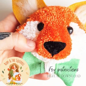 以下が含まれることがあります： オレンジと白の手作りのポンポン製のキツネのおもちゃのクローズアップ。黒い目と鼻をしています。キツネは緑色のスカーフを巻いており、手で持たれています。画像には「Fox instructions DIGITAL DOWNLOAD」というテキストが含まれています。