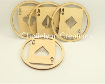May include: Four wooden coasters with a circular design. Each coaster features a different playing card suit: spades, clubs, diamonds, and hearts. The suits are cut out of the center of the coasters, revealing the wood underneath.
