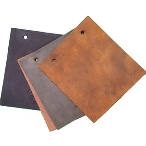 May include: Three pieces of leather in different colors and textures. The largest piece is a light brown leather with a smooth surface. The medium piece is a dark gray leather with a slightly textured surface. The smallest piece is a black leather with a smooth surface.