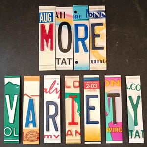 May include: A colorful sign spelling out "MORE VARIETY" using vintage license plates. The plates are arranged vertically and feature a variety of colors, including red, blue, green, yellow, and black.