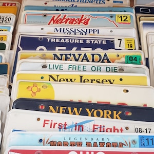 May include: A collection of vintage license plates from different US states. The plates are arranged in rows and columns, with the state names and slogans visible. Some of the plates are faded or worn, while others are in good condition.