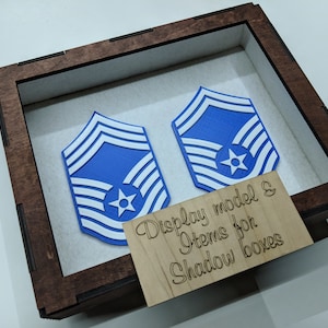 May include: Two blue and white 3D printed military rank insignia in a wooden shadow box with a sign that reads "Display model & Items for Shadow boxes".