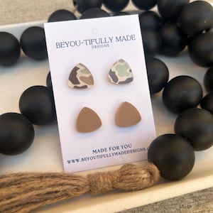 May include: A pair of earrings on a white card with the text "BEYOU-TIFULLY MADE DESIGNS". The earrings are triangular, with one pair featuring a camouflage pattern and the other pair in a solid tan color. Black beads are in the background.