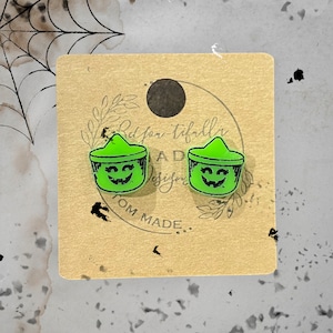 May include: A pair of green and black Halloween-themed earrings featuring a jack-o'-lantern design. The earrings are on a brown card with the text "Redfor-tiffally Designs" and "Tom Made".