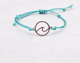 Könnte beinhalten: Ein türkisfarbenes Armband aus Schnur mit einem silbernen Anhänger in Wellenform.