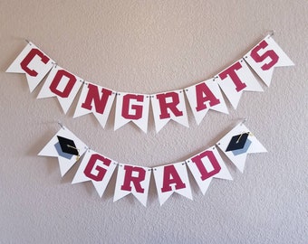 May include: White graduation banner with red letters spelling "Congrats Grad" with black graduation caps on each end.