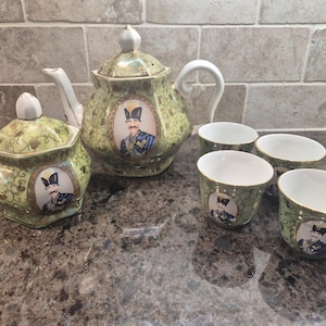 May include: A tea set featuring a teapot, a lidded sugar bowl, and three cups. Each piece is light green with a gold vine pattern and a central oval portrait of a man in a military uniform. The teapot and sugar bowl have white lids.