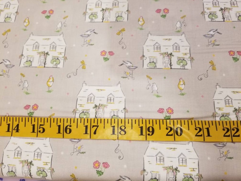 May include: A beige fabric with a repeating pattern of white houses, birds, flowers, and dragonflies. A yellow measuring tape is placed across the bottom of the fabric, showing measurements from 14 to 22 inches.