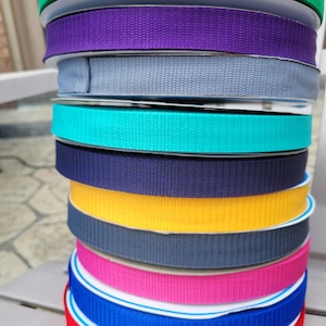 May include: A stack of colourful webbing straps in various colours, including green, purple, grey, turquoise, navy blue, yellow, dark grey, pink, blue, and red.