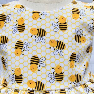 May include: White fabric with a repeating pattern of yellow honeycomb and black and yellow bees.