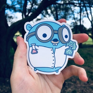 May include: A blue and white sticker of a cartoon gopher wearing glasses and a lab coat, holding a beaker in each hand. The gopher is smiling and has a friendly expression.