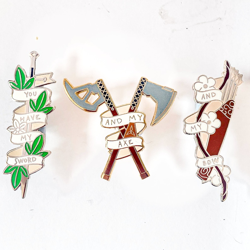 May include: Three enamel pins featuring a sword, axe, and bow and arrow. Each pin has a white banner with text that reads "You have my sword", "And my axe", and "And my bow".