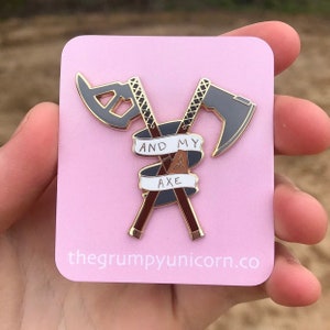 May include: Gold and black enamel pin with two crossed axes and a banner that reads "And My Axe".