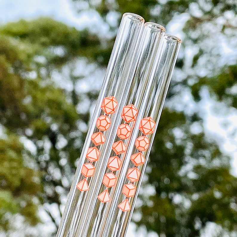 Pu&ograve; includere: Set di tre cannucce da bere in vetro con un design geometrico rosa e bianco. Le cannucce sono trasparenti e hanno un design rosa e bianco a forma di dadi.