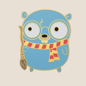 Op de afbeelding: Een blauwe emaille pin met een stripfiguur met een ronde bril, een bliksemschicht litteken en een rood-gele sjaal. Het personage houdt een bezem vast. De pin heeft een gouden omtrek.