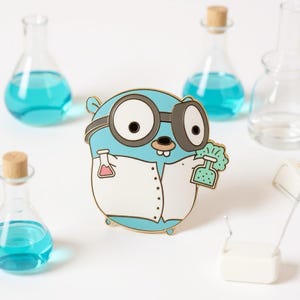 Può includere: Spilla a cartone animato azzurra raffigurante un gopher con occhiali e camice da laboratorio, che tiene in mano un becher. La spilla è circondata da piccole bottiglie di vetro con liquido blu e tappi di sughero. La spilla ha un contorno dorato.