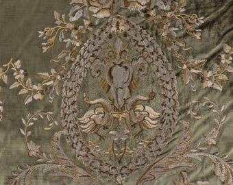 May include: A close-up of a green fabric with an intricate embroidered design featuring a floral pattern and two stylised birds. The embroidery is in shades of silver and gold.