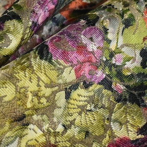 May include: A close-up of a fabric with a floral pattern. The fabric is a gold color with a textured surface. The flowers are pink, red, and green.