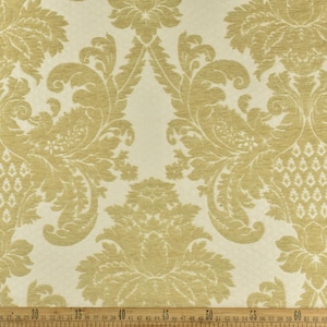 May include: A white fabric with a gold damask pattern. The pattern features intricate floral designs and swirls.