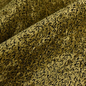 May include: Close-up of a textured fabric with a pattern of black speckles on a golden-olive background. The fabric is folded, showing the texture and depth of the material. The overall appearance suggests a decorative textile.