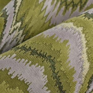 Op de afbeelding: Close-up van een gevouwen stof met een getextureerd zigzagpatroon. De stof heeft tinten groen, olijf en grijs, waardoor een gelaagd, abstract ontwerp ontstaat. Het materiaal lijkt zacht en is mogelijk geschikt voor bekleding of woondecoratie.