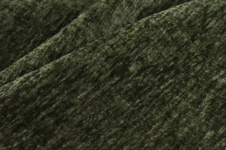 May include: Close-up of a textured fabric in a deep green colour. The fabric has a slightly fuzzy texture and a subtle sheen.