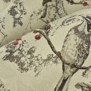 Könnte beinhalten: Ein beigefarbener Stoff mit einem braunen und weißen Vogelmuster. Der Vogel sitzt auf einem Ast mit roten Beeren. Der Stoff hat eine strukturierte, gewebte Optik.