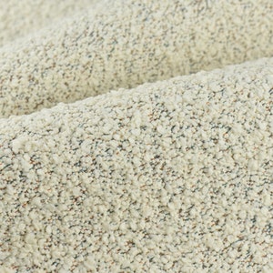 Puede incluir: Primer plano de una tela texturizada con fondo crema y motas de azul y marrón.