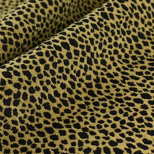 May include: A close-up of a fabric with a leopard print pattern. The fabric is a light brown colour with black spots. The fabric has a textured surface.