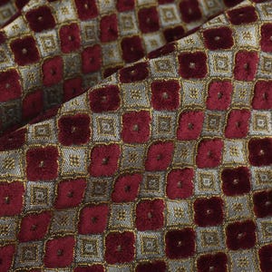May include: Close-up of folded fabric featuring a repeating pattern of burgundy squares within a silver and gold grid. The fabric has a textured, possibly velvet, appearance.