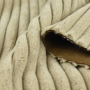 K&ouml;nnte beinhalten: Nahaufnahme eines beigefarbenen Cordstoffs mit brauner R&uuml;ckseite. Der Stoff hat eine weiche, pl&uuml;schige Textur und ein geripptes Muster.