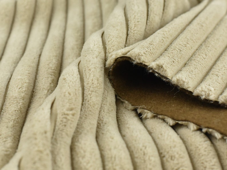 K&ouml;nnte beinhalten: Nahaufnahme eines beigefarbenen Cordstoffs mit brauner R&uuml;ckseite. Der Stoff hat eine weiche, pl&uuml;schige Textur und ein geripptes Muster.