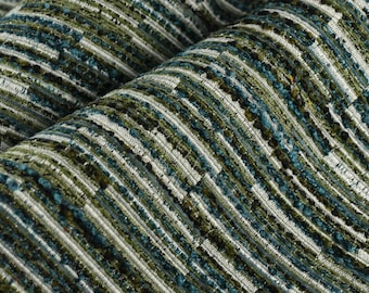 Op de afbeelding: Close-up van een textielstof met een geweven patroon. De stof heeft een mix van kleuren, waaronder blauwgroen, olijfgroen en wit, waardoor een gestreept effect ontstaat. Het materiaal lijkt dik en duurzaam, geschikt voor bekleding of woondecoratie.