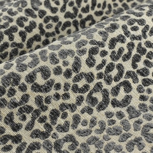 Könnte beinhalten: Nahaufnahme eines beigefarbenen Stoffes mit einem schwarzen Leopardenmuster. Der Stoff hat eine strukturierte Oberfläche.