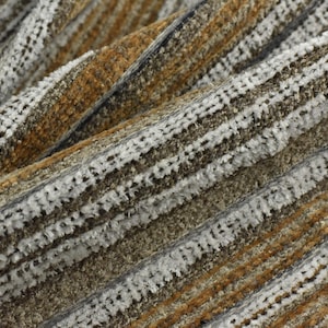 Pode incluir: Close-up de um tecido texturizado com um padrão listrado. O tecido apresenta faixas alternadas de cores branca, marrom e bege, criando um design visualmente interessante. O material parece macio e felpudo.