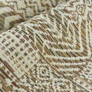 May include: Close-up of a cream-colored rug with a geometric pattern in shades of brown, beige, and black. The rug has a textured surface and a woven design.