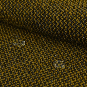 Op de afbeelding: Close-up van een textuurdoek met een donkerbruin en mosterdgeel patroon. Waterdruppels zijn zichtbaar op het oppervlak van de stof.