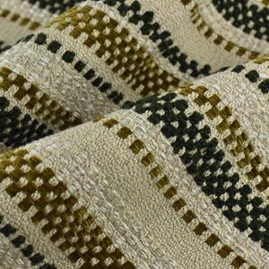 Pode incluir: Close-up de um tecido tecido com superfície texturizada. O tecido apresenta um padrão repetitivo de quadrados e linhas verde-oliva e verde-escuro sobre um fundo bege. O tecido está dobrado, mostrando a textura e profundidade da tecelagem.