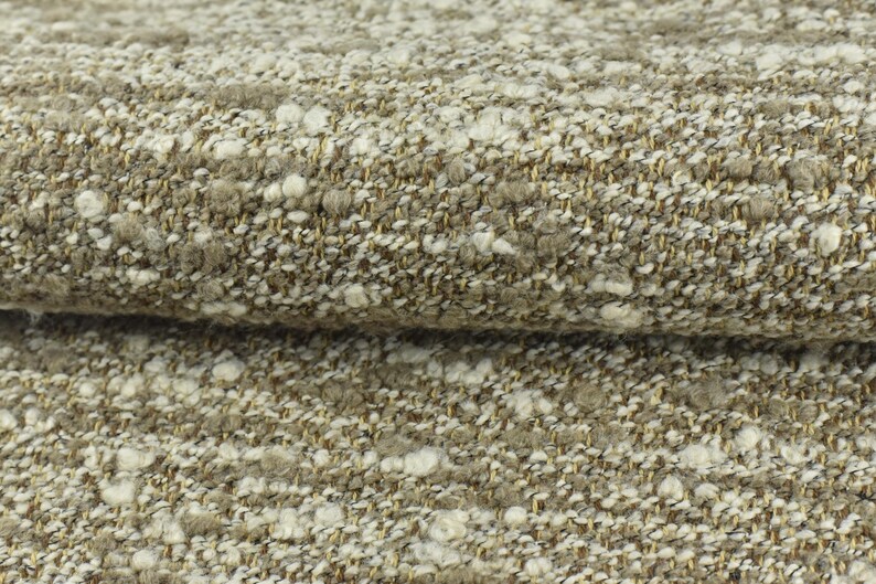 May include: Close-up of a textured fabric with a beige background and white flecks. The fabric has a subtle shimmer and a soft, fuzzy texture.