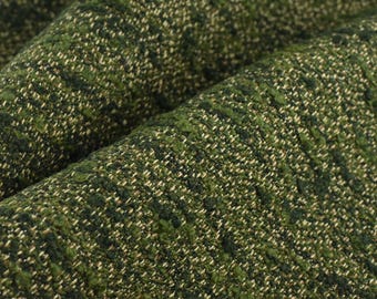 May include: Close-up of a textured fabric with a woven pattern. The fabric is primarily green with flecks of lighter green and beige, creating a speckled appearance. The material is folded, showing depth and texture.