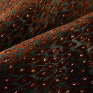 May include: Close-up of a textured fabric with a repeating diamond pattern. The fabric features a dark teal background with rust-coloured diamond shapes. The fabric is folded, highlighting the texture and depth of the material.