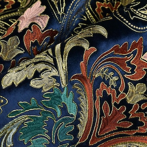 May include: Close-up of a navy blue fabric with an ornate embroidered design. The embroidery features gold, rust, pink, and green floral and leaf patterns. The fabric has a velvety texture and a rich, luxurious appearance.