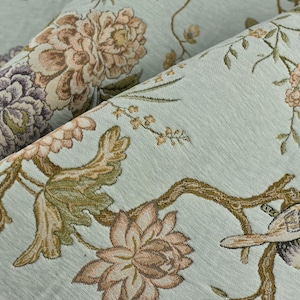 Puede incluir: Primer plano de una tela azul claro con un estampado floral y de pájaros. El diseño presenta grandes flores detalladas en tonos marrón, morado y rosa, junto con pájaros posados en ramas. La tela tiene un aspecto texturizado.