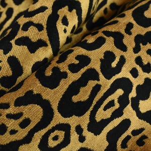 Könnte beinhalten: Nahaufnahme eines Stoffes mit einem schwarzen und goldenen Leopardenmuster. Der Stoff hat eine weiche, samtige Textur.