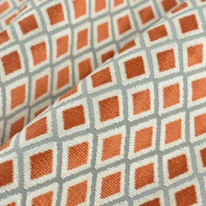 May include: A close-up of a fabric with a geometric pattern. The fabric has a light grey background with a repeating pattern of orange squares.