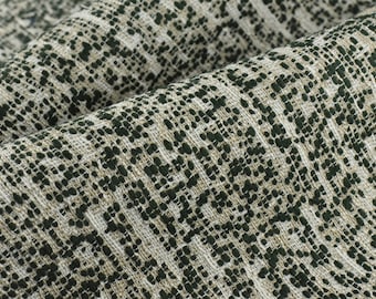 May include: Close-up of a textured fabric with a repeating pattern of small dark green dots on a light beige background.