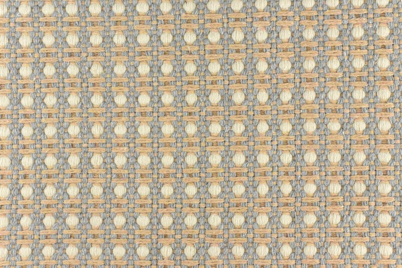 May include: A close-up of a woven fabric with a light brown and gray pattern. The fabric has a textured surface and a repeating pattern of small circles.