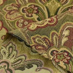 May include: Close-up of a folded fabric with a detailed paisley pattern. The fabric features a blend of olive green, burgundy, and gold colors. The design includes floral and curved elements, creating a vintage aesthetic.