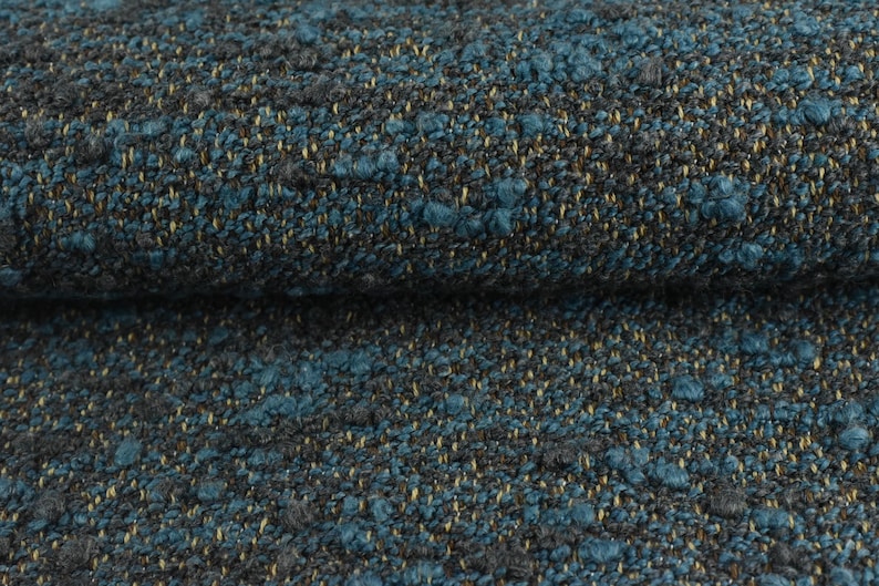 May include: Close-up of a textured fabric with a mix of teal, gray, and gold threads. The fabric has a nubby, woven appearance, with small, raised tufts of teal. The overall effect is a rich, dimensional textile.